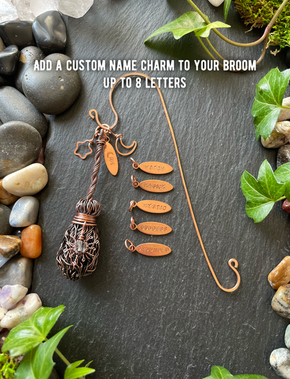 Decorative broom with customizable name charms on a stone surface with plants.