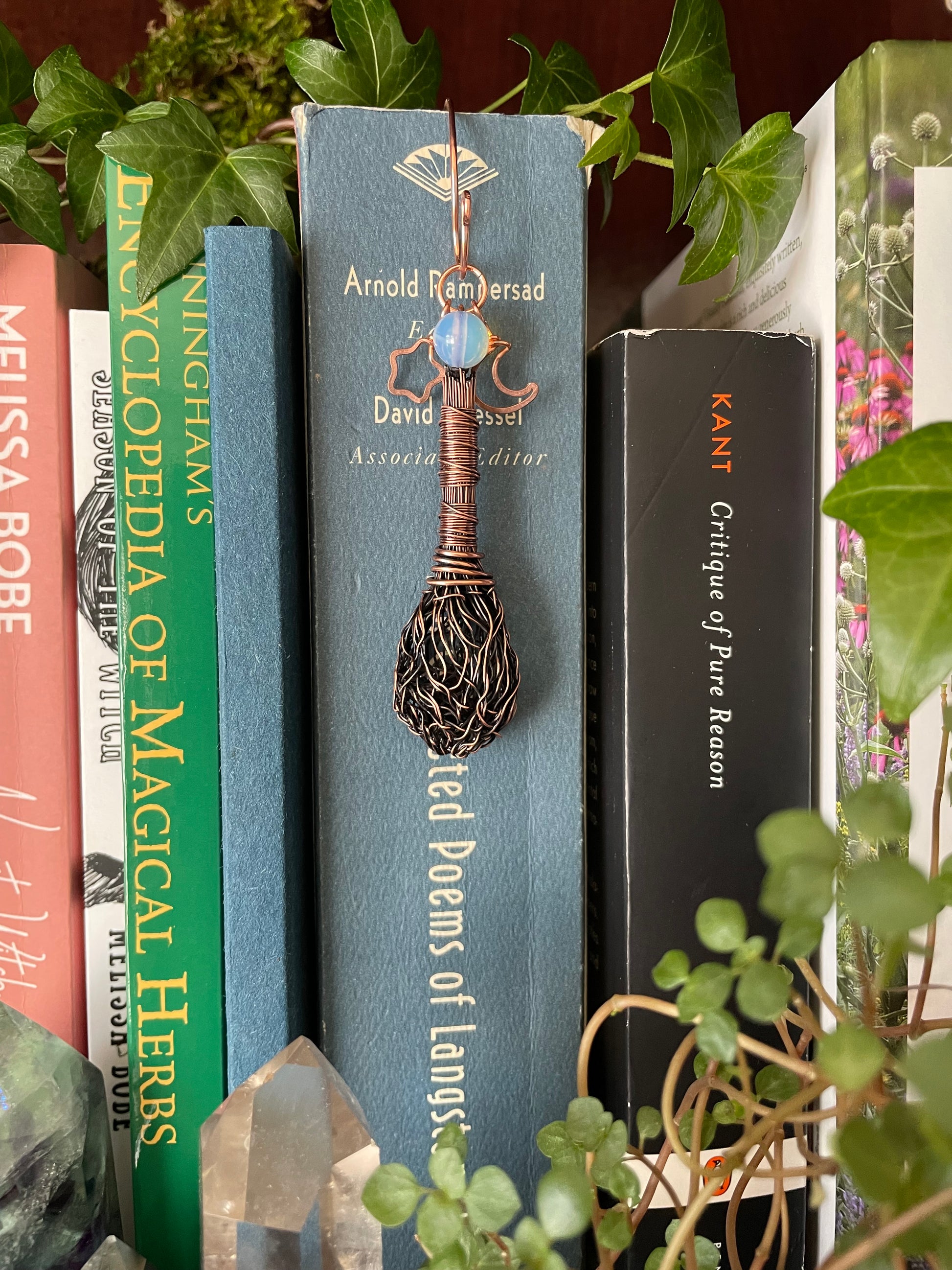 Books on a shelf with a decorative broom on top, surrounded by greenery