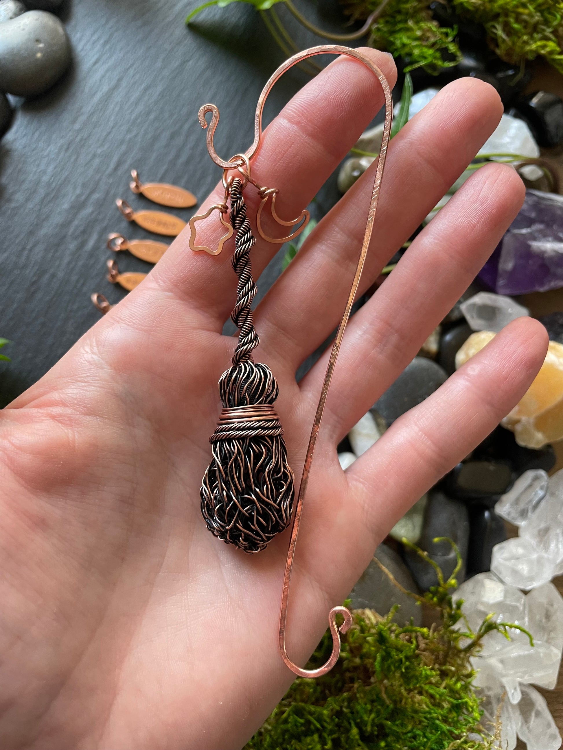 A miniature wire broom attached to a copper bookmark being held in hand