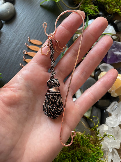 A miniature wire broom attached to a copper bookmark being held in hand