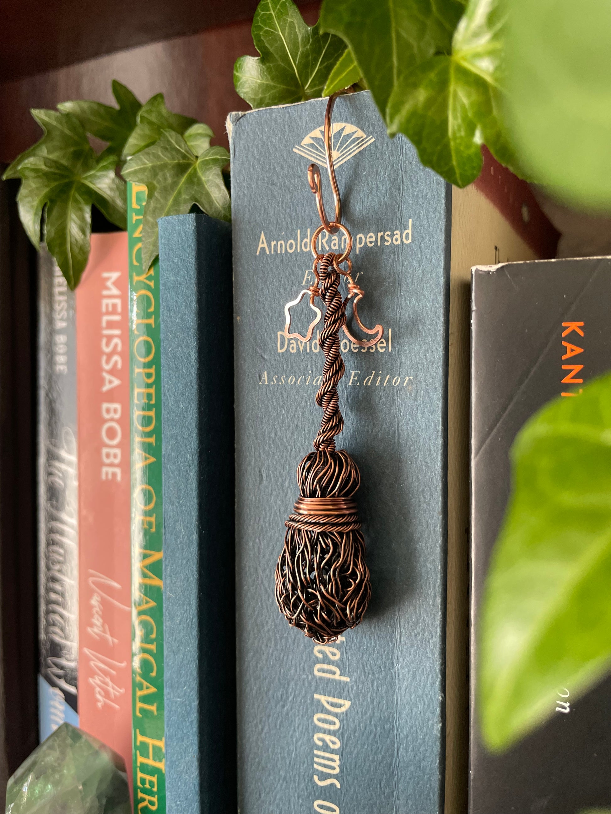 A miniature copper broom bookshelf charm attached to a book on a bookshelf