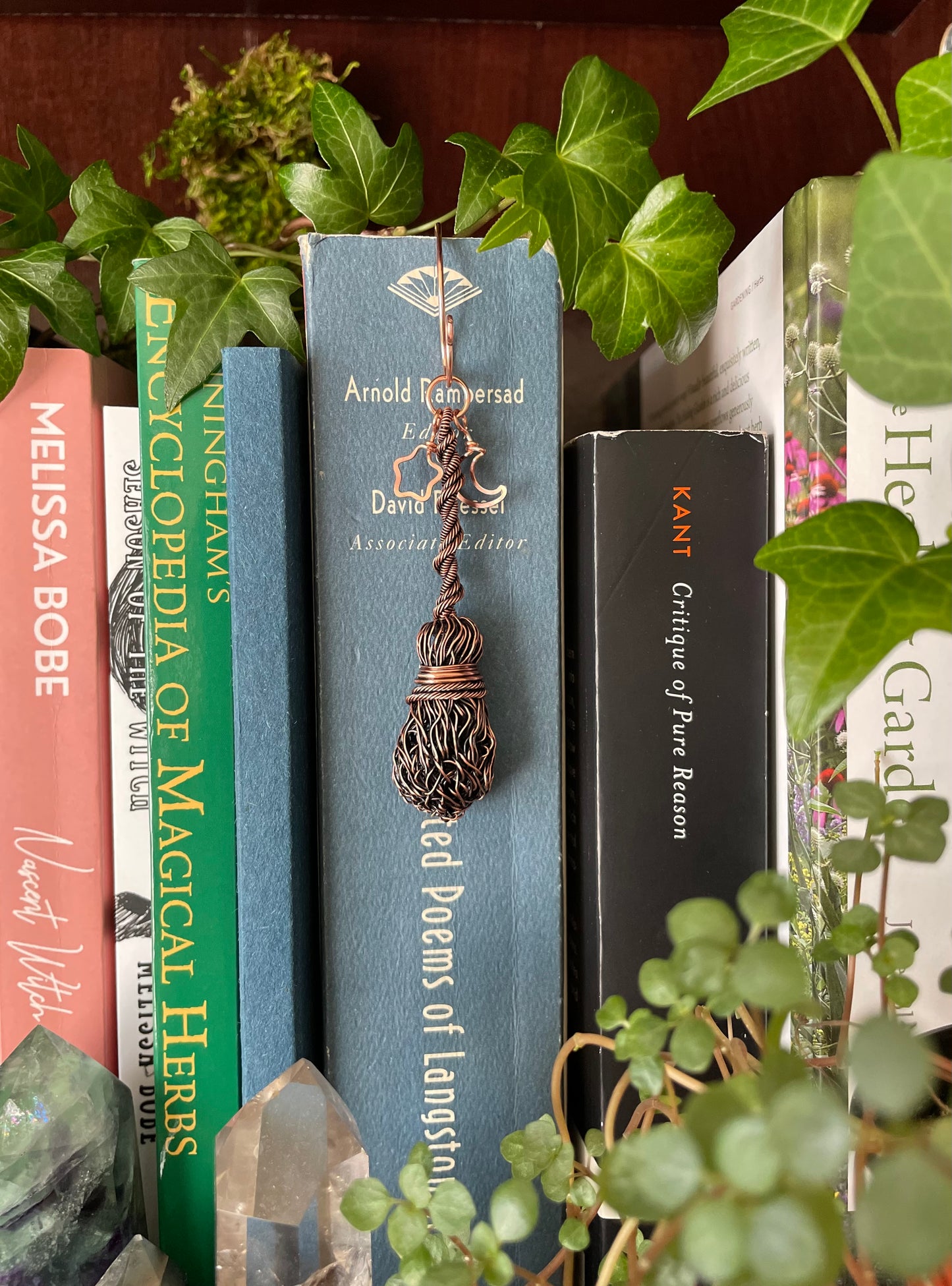Miniature copper broom bookmark charm attached to books on a shelf