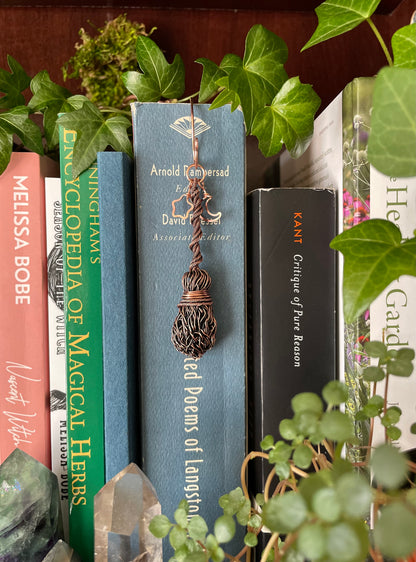Miniature copper broom bookmark charm attached to books on a shelf