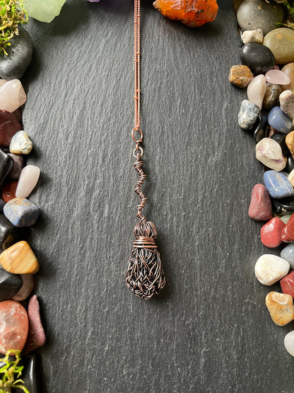 Decorative broomstick pendant on a dark stone surface with pebbles around