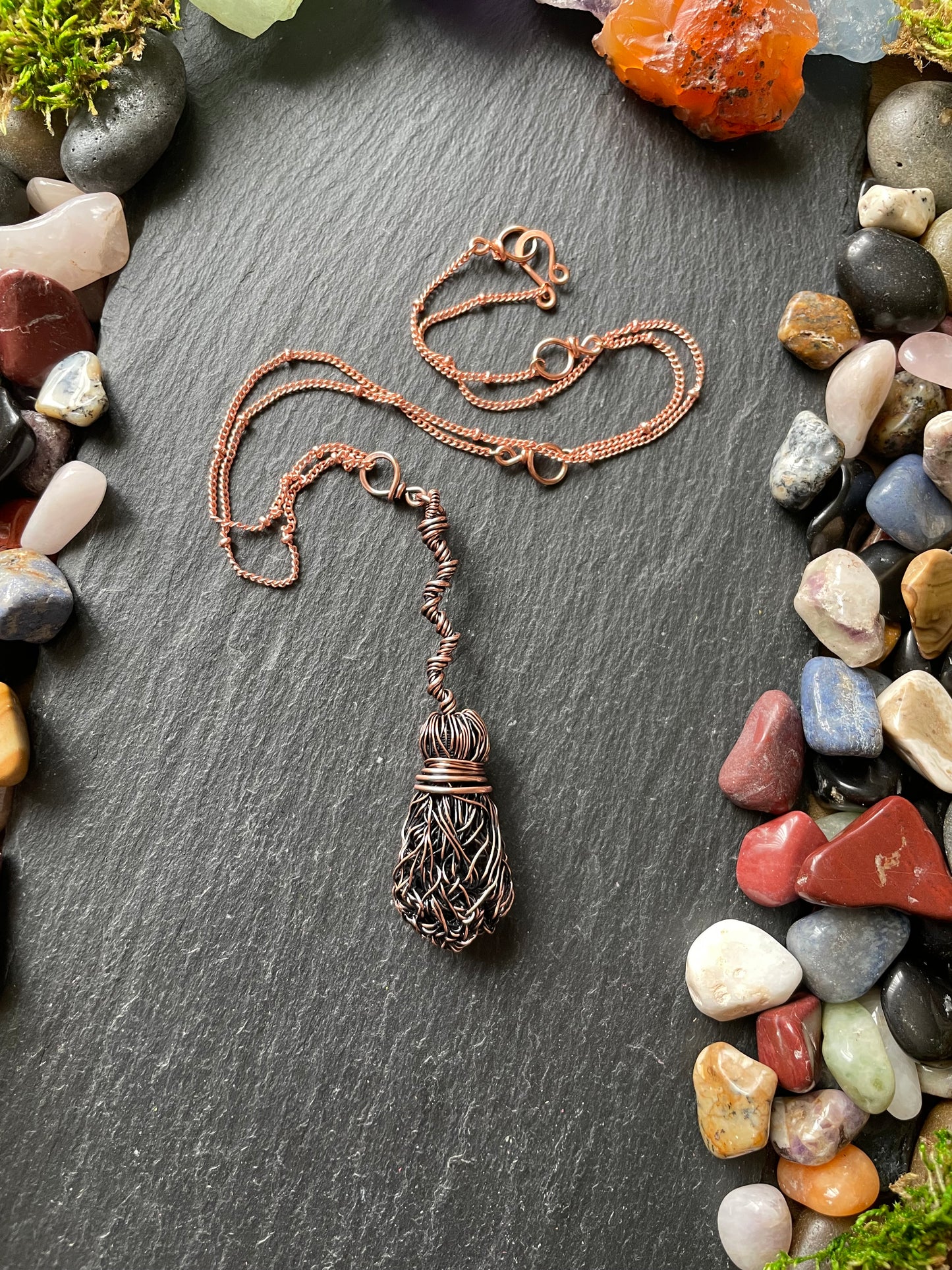 Copper necklace on a dark surface with pebbles and plants