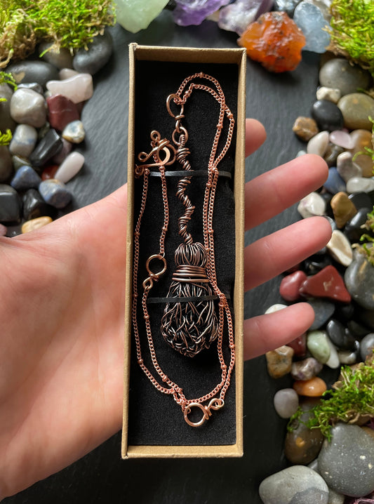 Copper necklace in a box held by a hand with a natural stone background