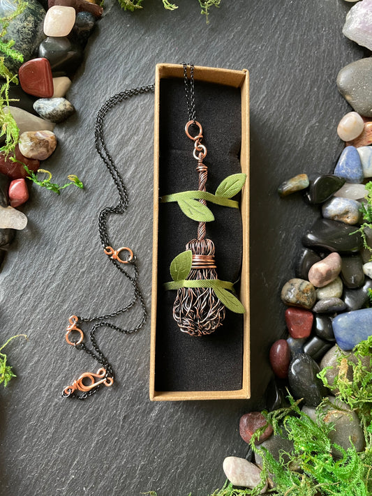 Broom pendant held in a box with green leaf ribbon on a stone surface
