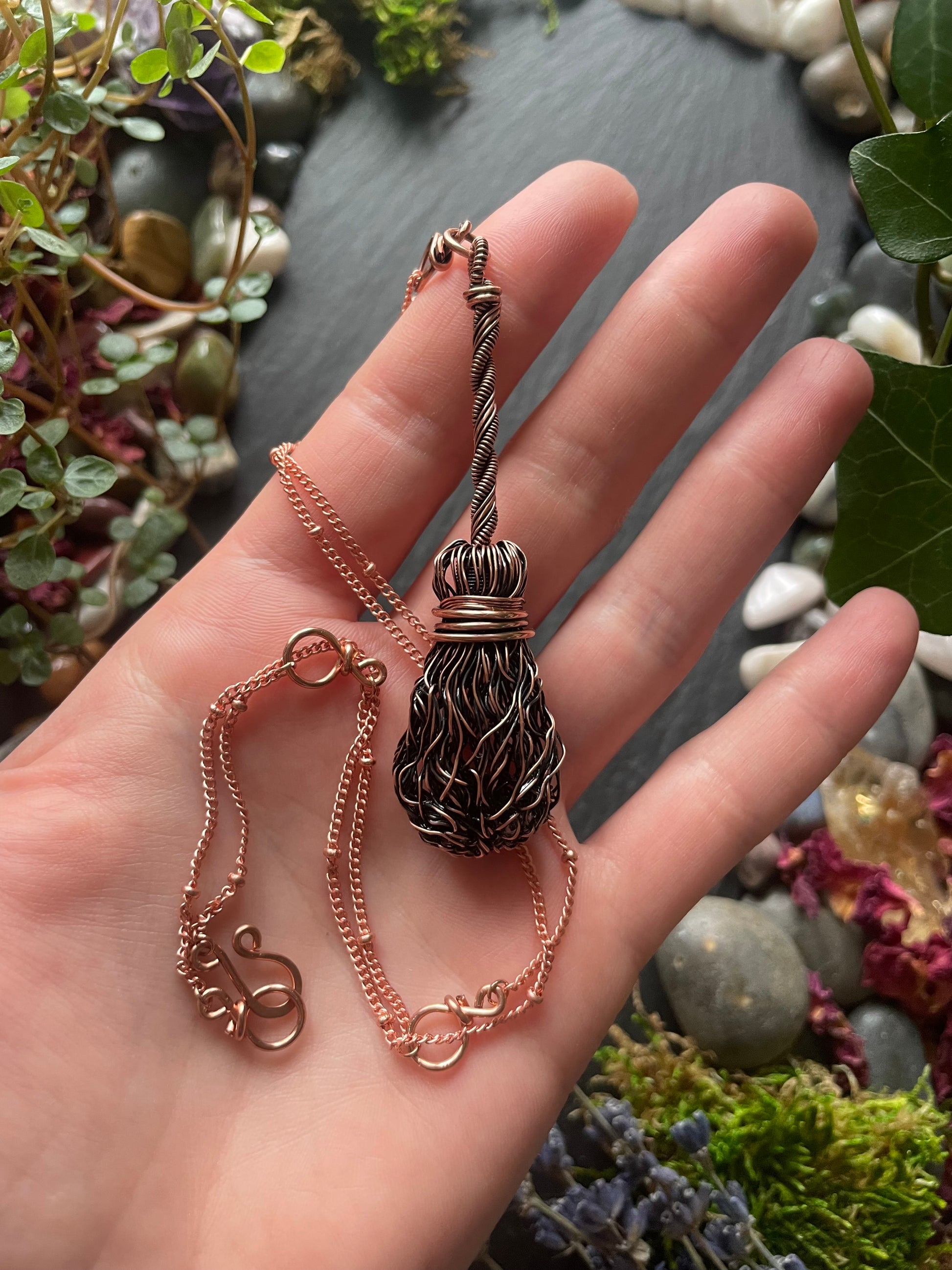 Hand holding a copper broom necklace against a natural background