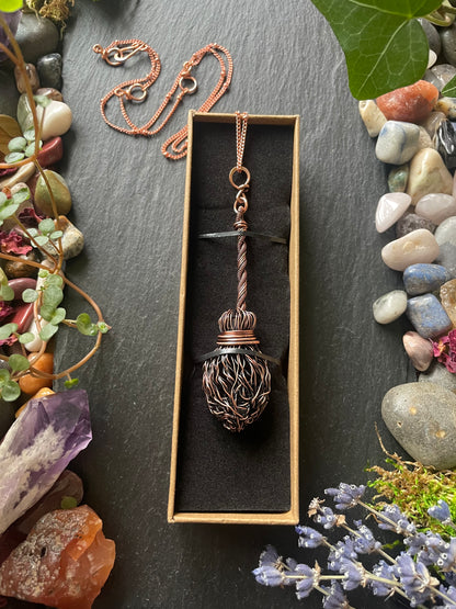 Decorative copper broom necklace in a box with natural elements around