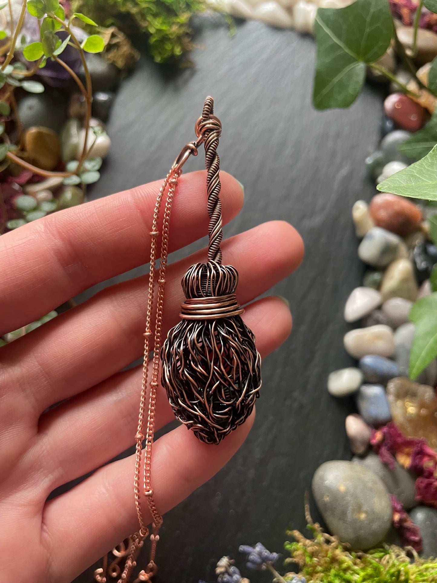 Hand holding a decorative necklace with a detailed pendant against a natural background.