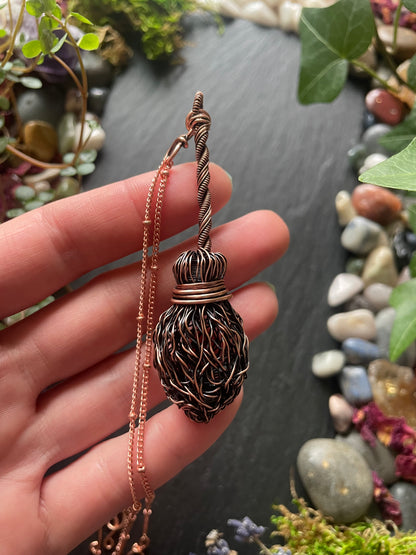 Hand holding a decorative necklace with a detailed pendant against a natural background.