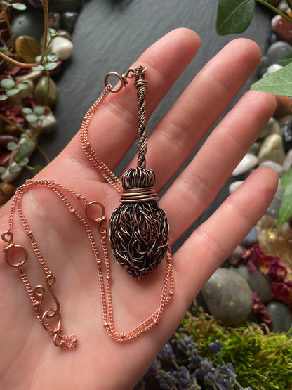 Copper broom necklace held in a hand with a natural background