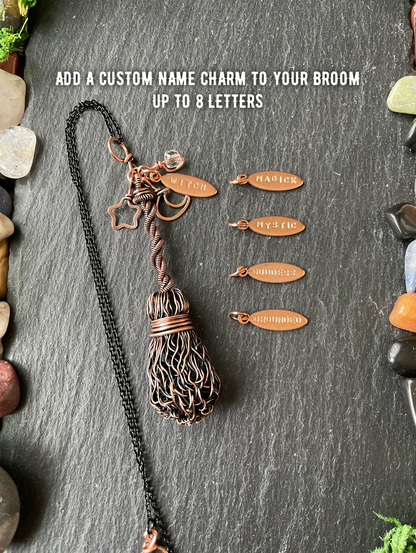 A handmade copper wire broom, displayed on a dark slate background with small engraved copper name charms and white text that reads 'ADD A CUSTOM NAME CHARM TO YOUR BROOM UP TO 8 LETTERS'.