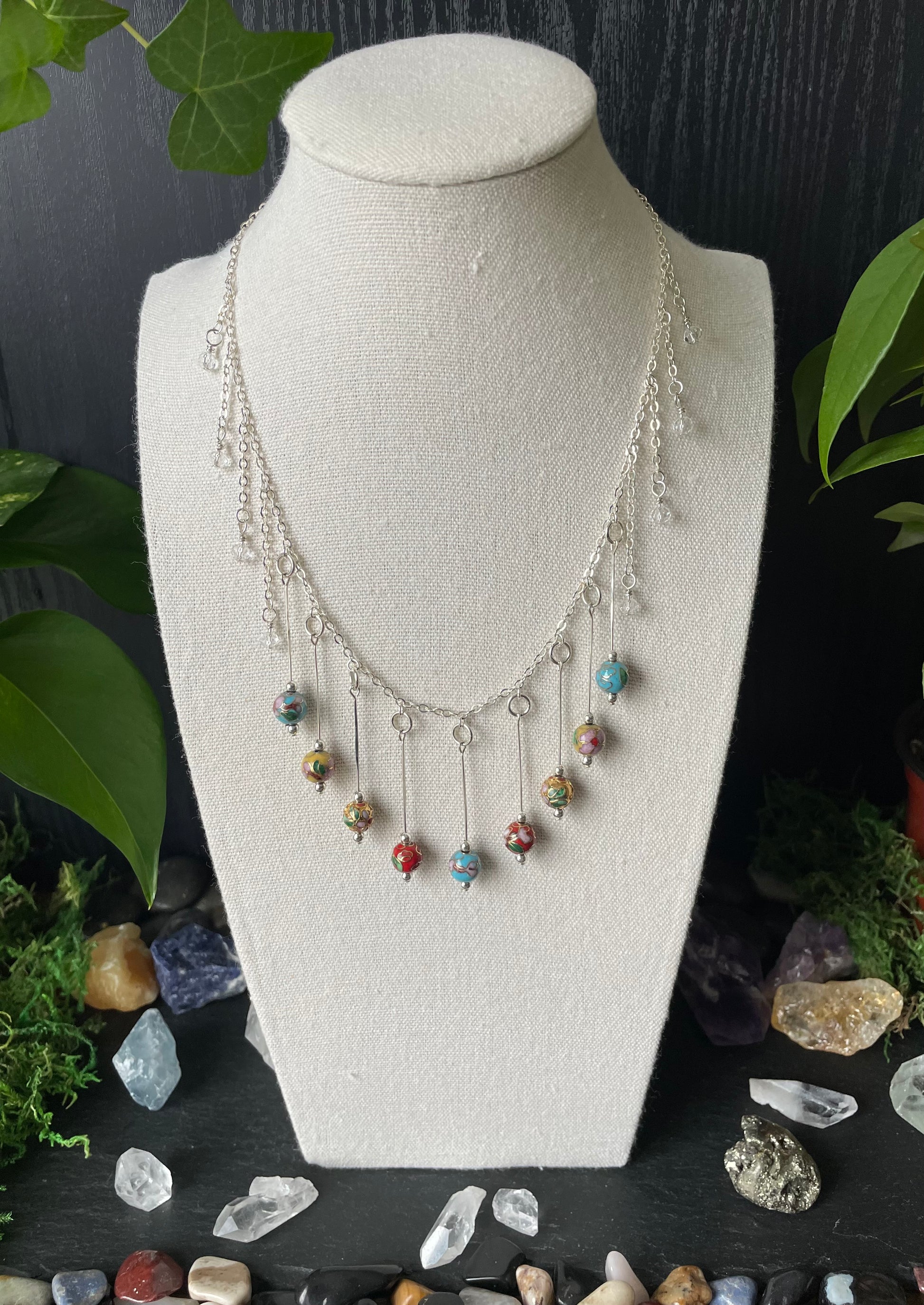 Necklace with colorful beads on a mannequin bust against a dark background with stones and plants.