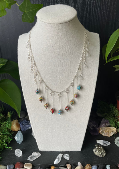 Necklace with colorful beads on a mannequin bust against a dark background with stones and plants.
