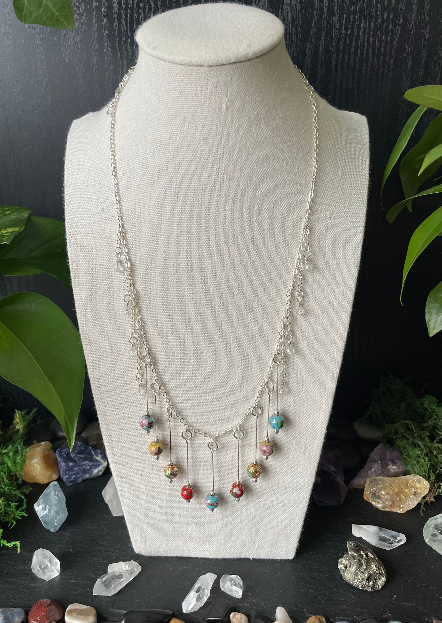 Necklace with colorful beads on a white bust against a dark background with crystals and plants.