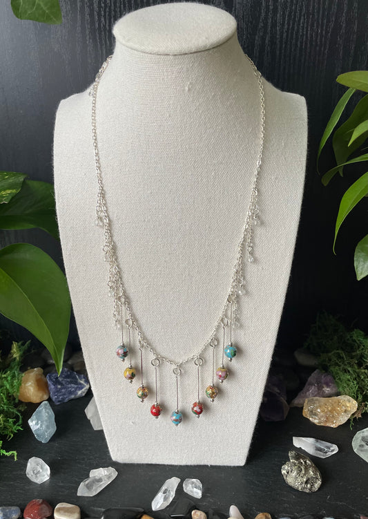 Necklace with colorful beads on a white bust against a dark background with crystals and plants.