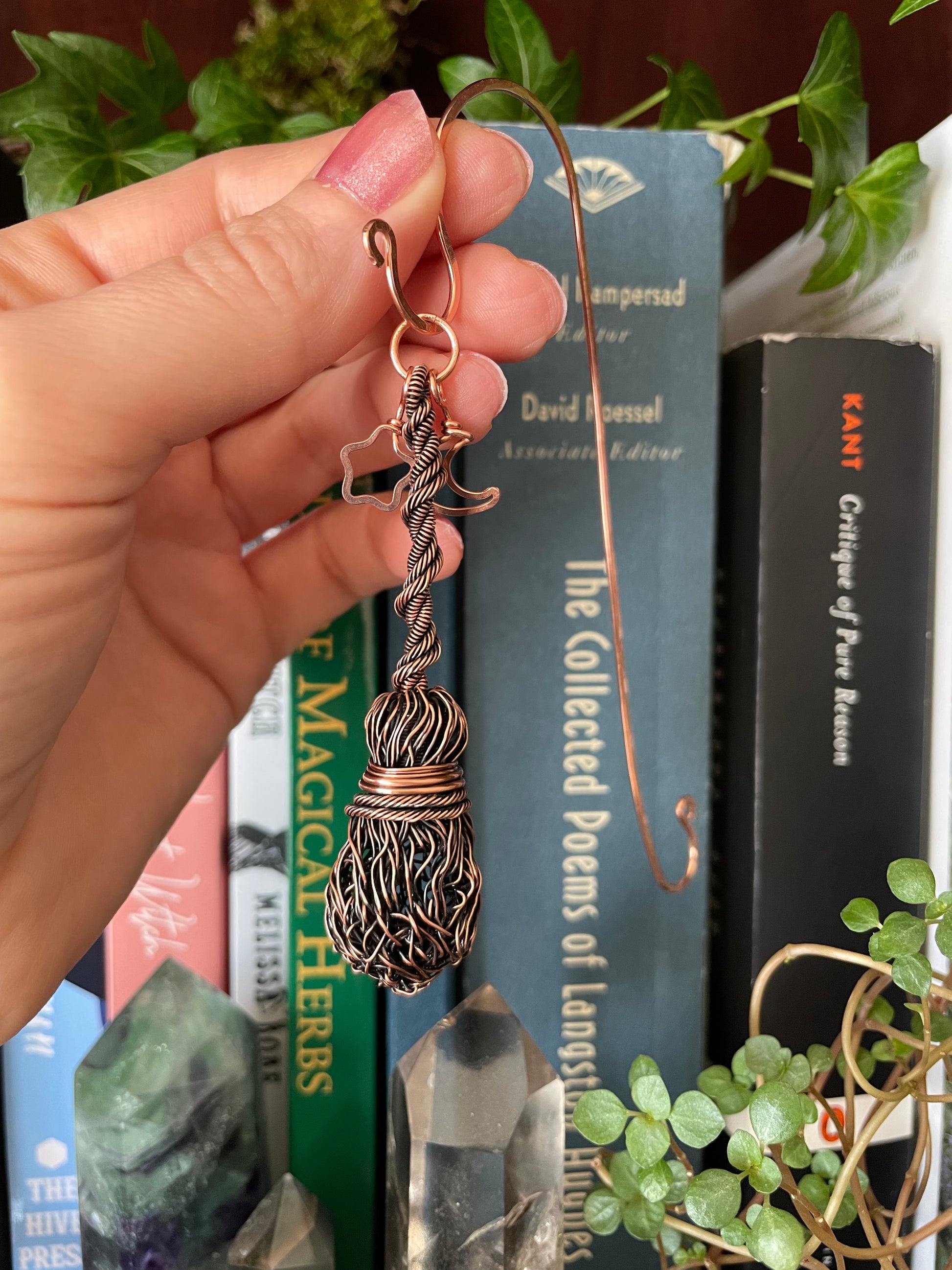 Copper wire sculpture held by a hand with books and plants in the background