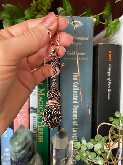 Copper wire sculpture held by a hand with books and plants in the background