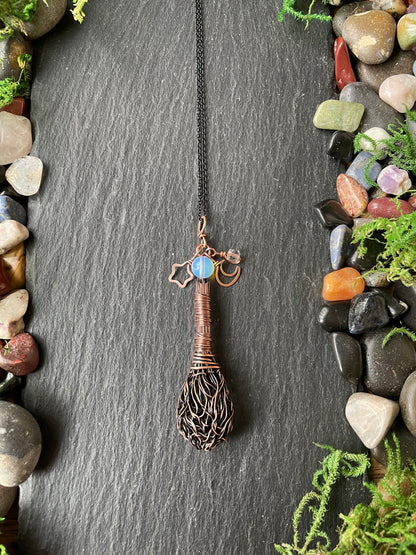 A handmade pendant necklace displayed on a dark slate background with decorative stones and greenery.