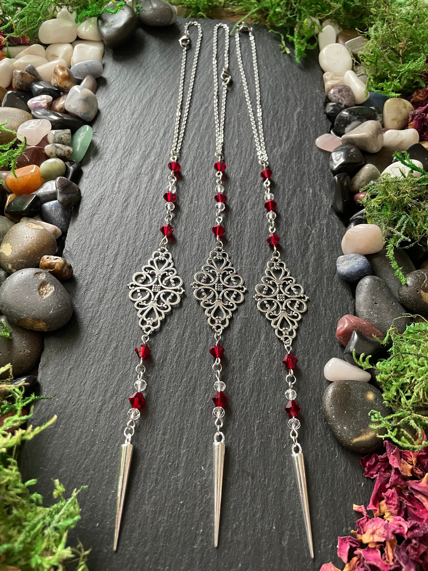 Car mirror charms with red beads on a dark surface surrounded by stones and plants
