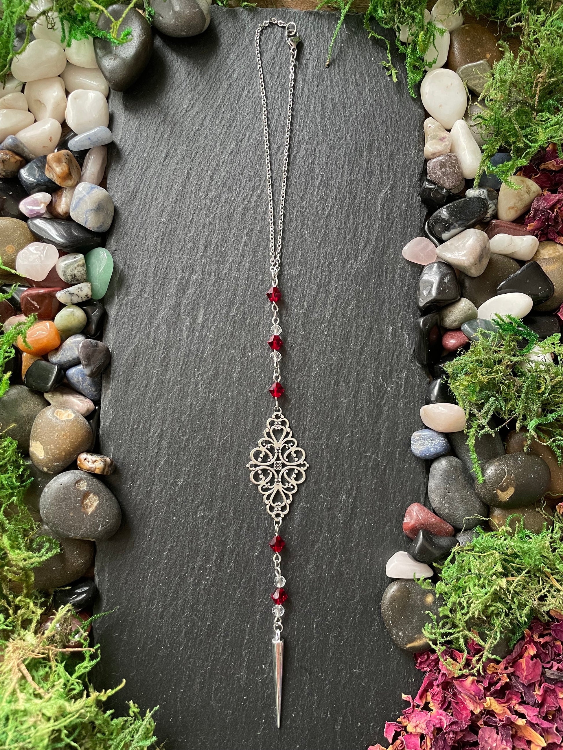 Car mirror charm with red beads on a dark slate stone surrounded by stones and moss