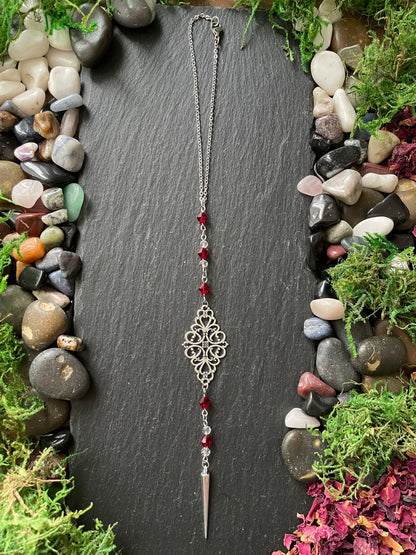Car mirror charm with red beads on a dark slate stone surrounded by stones and moss
