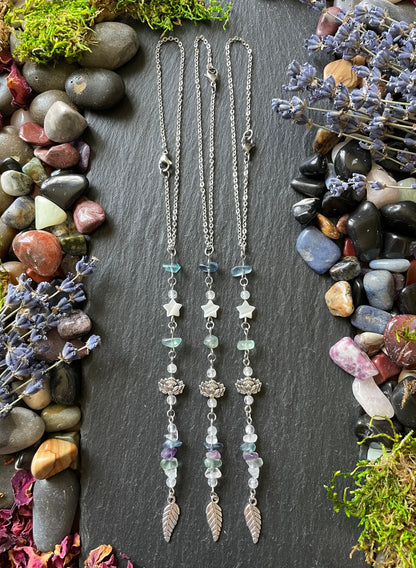 Three car charms with fluorite crystal beads, lotus flower beads, mother of pearl star beads, and leaf charms displayed on a stone slate surrounded by gems and moss