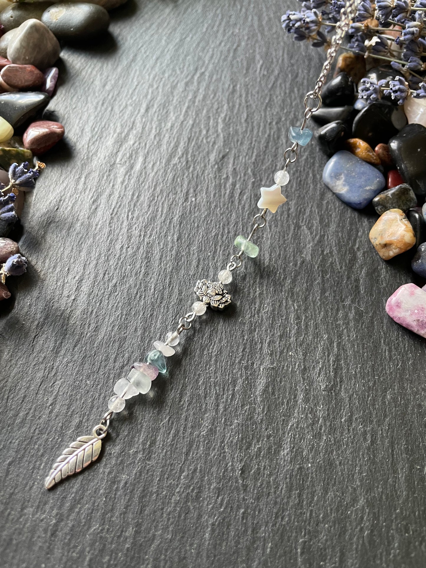 Car charm with blue, green, and purple fluorite crystal beads, silver lotus flower bead, mother of pearl star bead, and silver leaf charm displayed on a stone slate