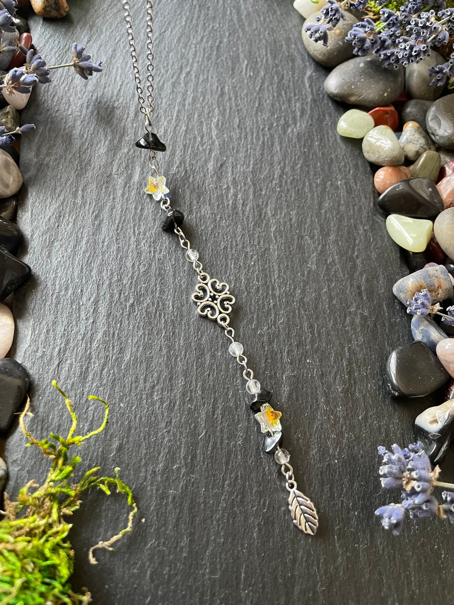 Car charm with obsidian crystal beads and star charms, placed on a stone slate near gemstones