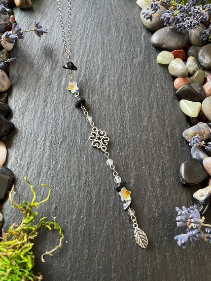 Car charm with obsidian crystal beads and star charms, placed on a stone slate near gemstones