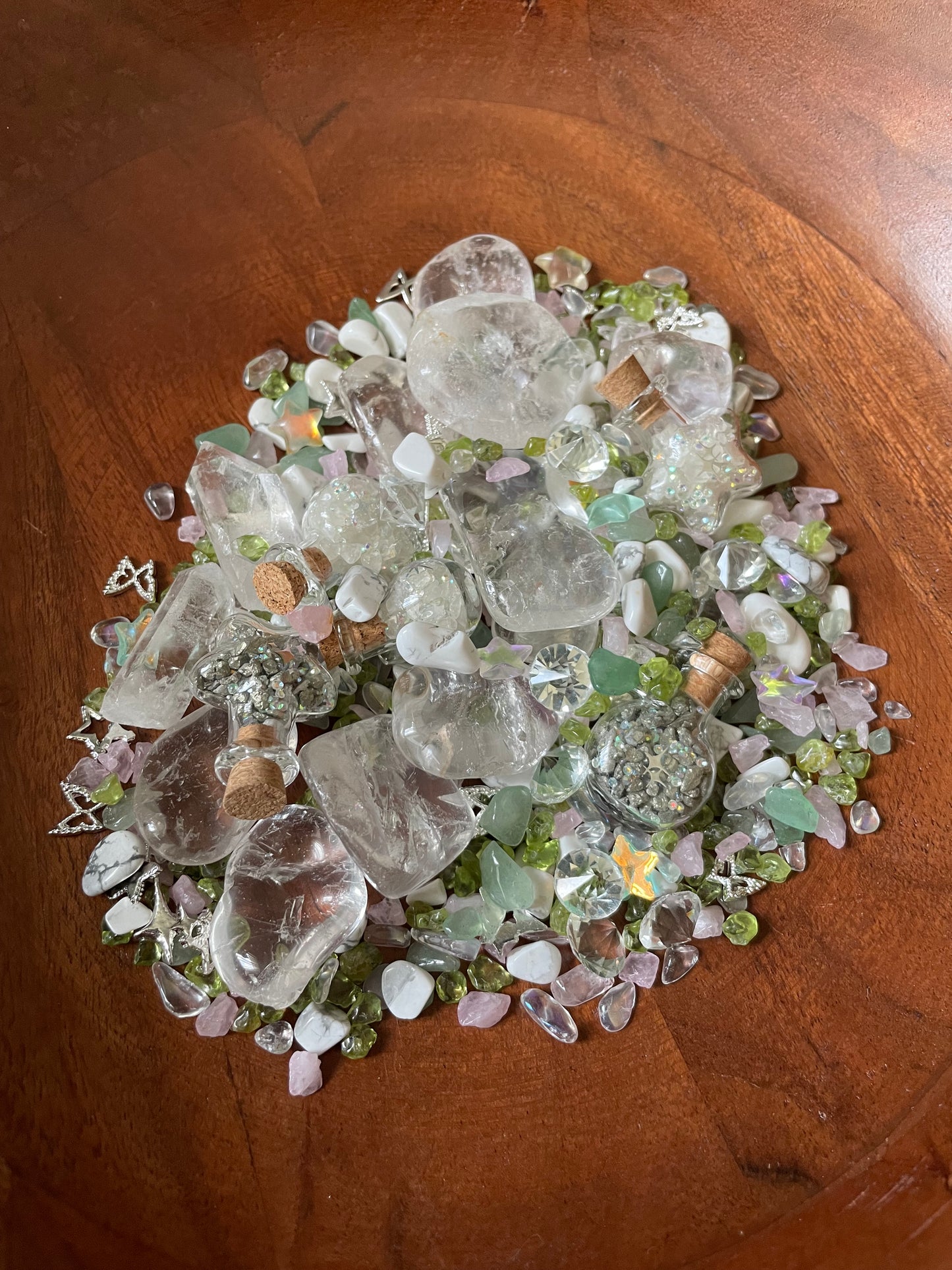A pile of assorted clear quartz crystal chunks and small pale green and arranged in the center of a round wooden bowl.