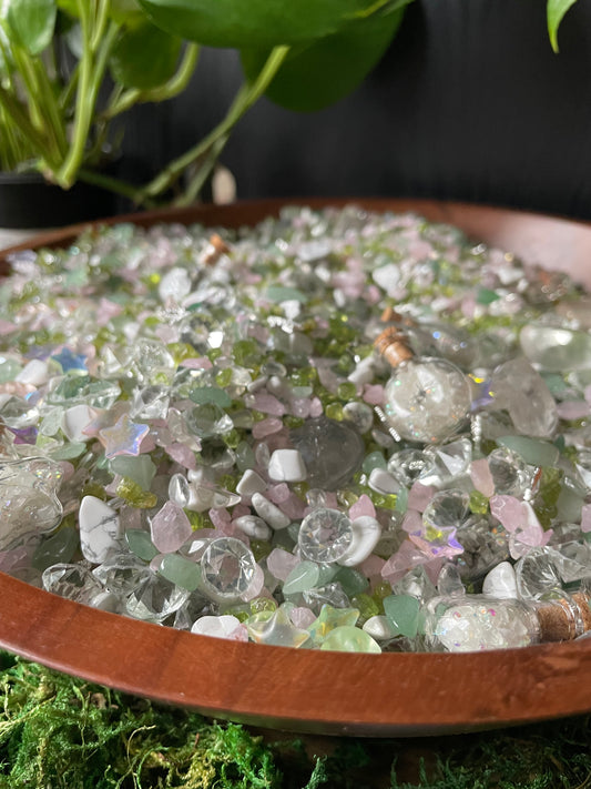 A close-up of pastel-colored gemstones, styled with green moss and plants.