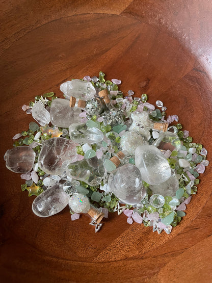 A pile of clear quartz crystal tumbled stones and small pale pink and green gems arranged in a wooden bowl.