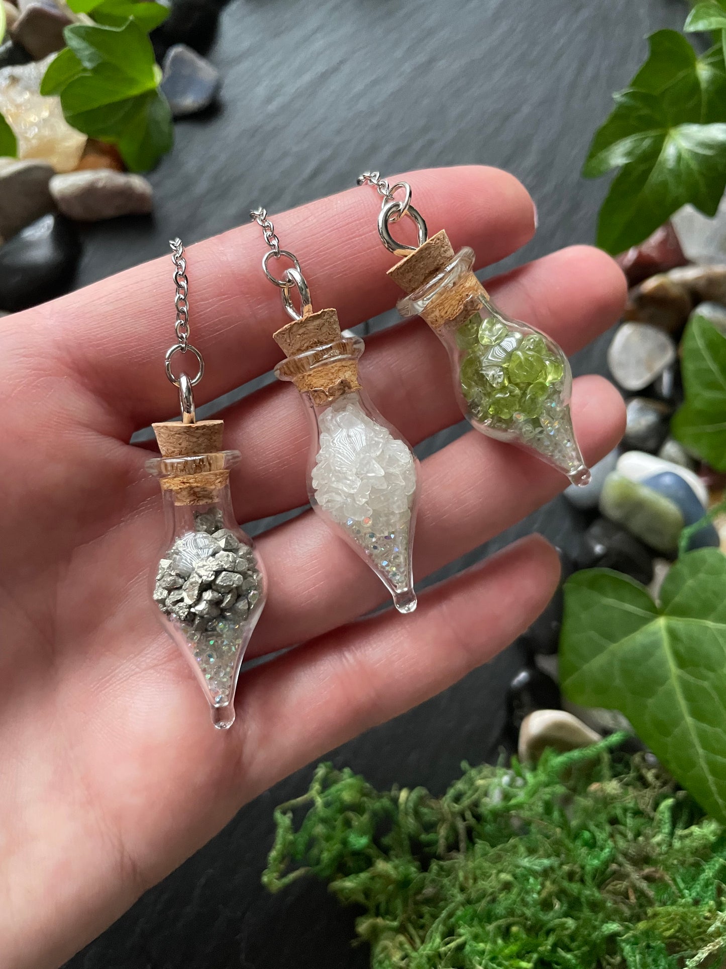 Hand holding three small glass containers with crystals against a natural background