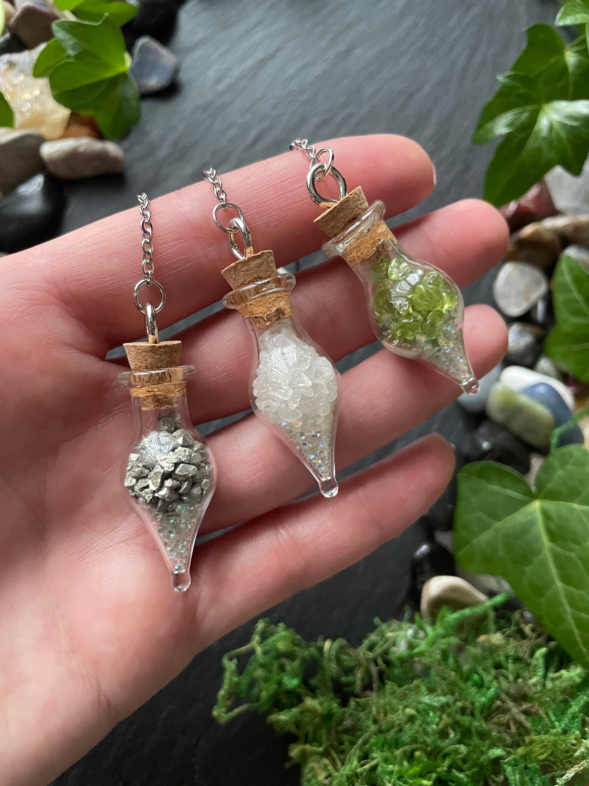 Hand holding three small glass containers with crystals against a natural background