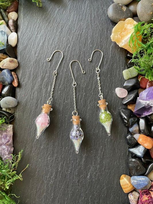 Colorful crystal plant charms on a dark slate surface with colorful stones and greenery.