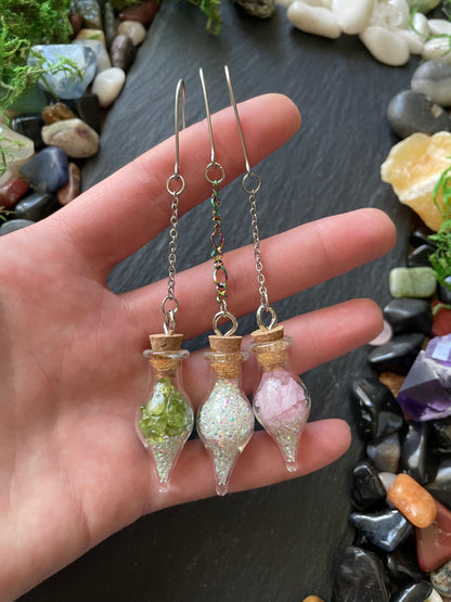 Hand holding small decorative glass bottles against a background of stones and crystals