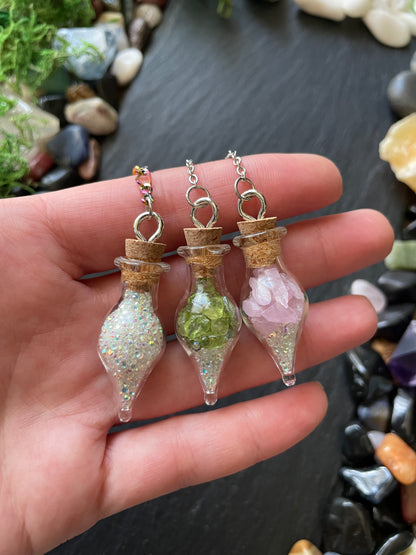Hand holding glass vial plant charms with a natural stone background