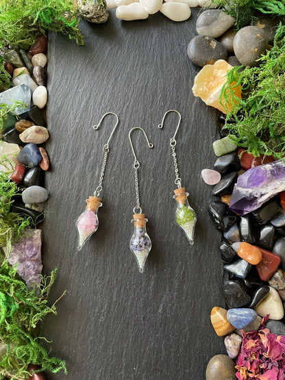 Crystal-themed plant charms on a dark slate surface with stones and moss around.
