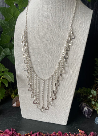 Silver necklace with star-shaped charms on a mannequin bust against a natural background.