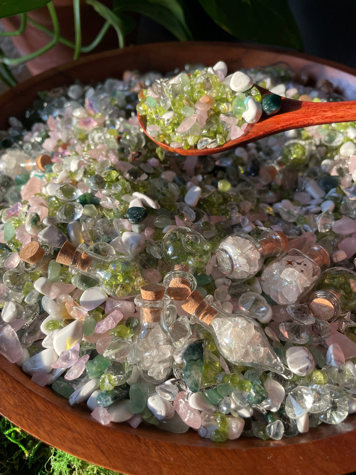 A wooden bowl filled with colorful decorative stones in clear, pink, green, and white, with a wooden spoon lifting a scoop of the stones.