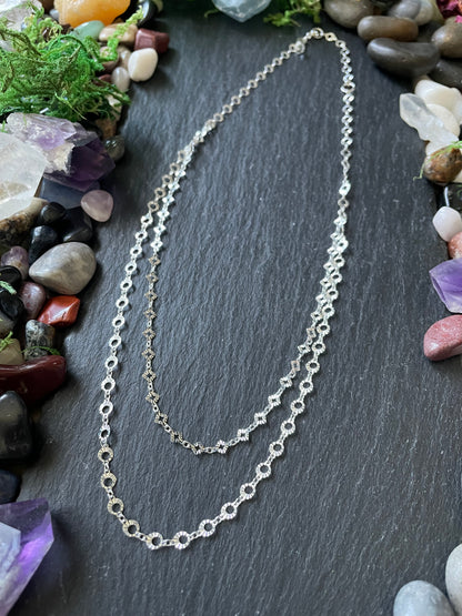 Silver chain necklace on a dark stone surface with stones and crystals around