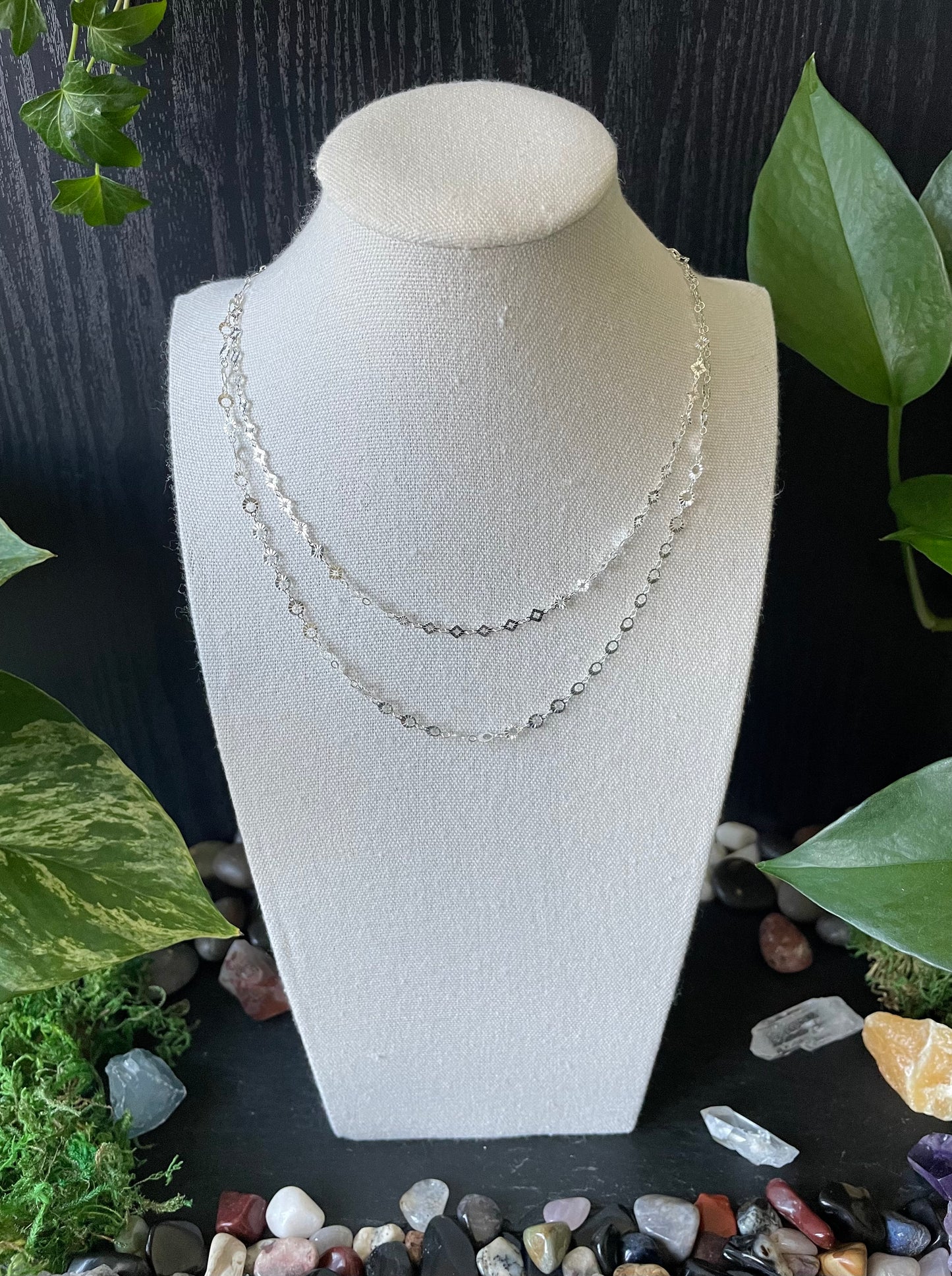 Necklace on a white bust with greenery and stones in the background