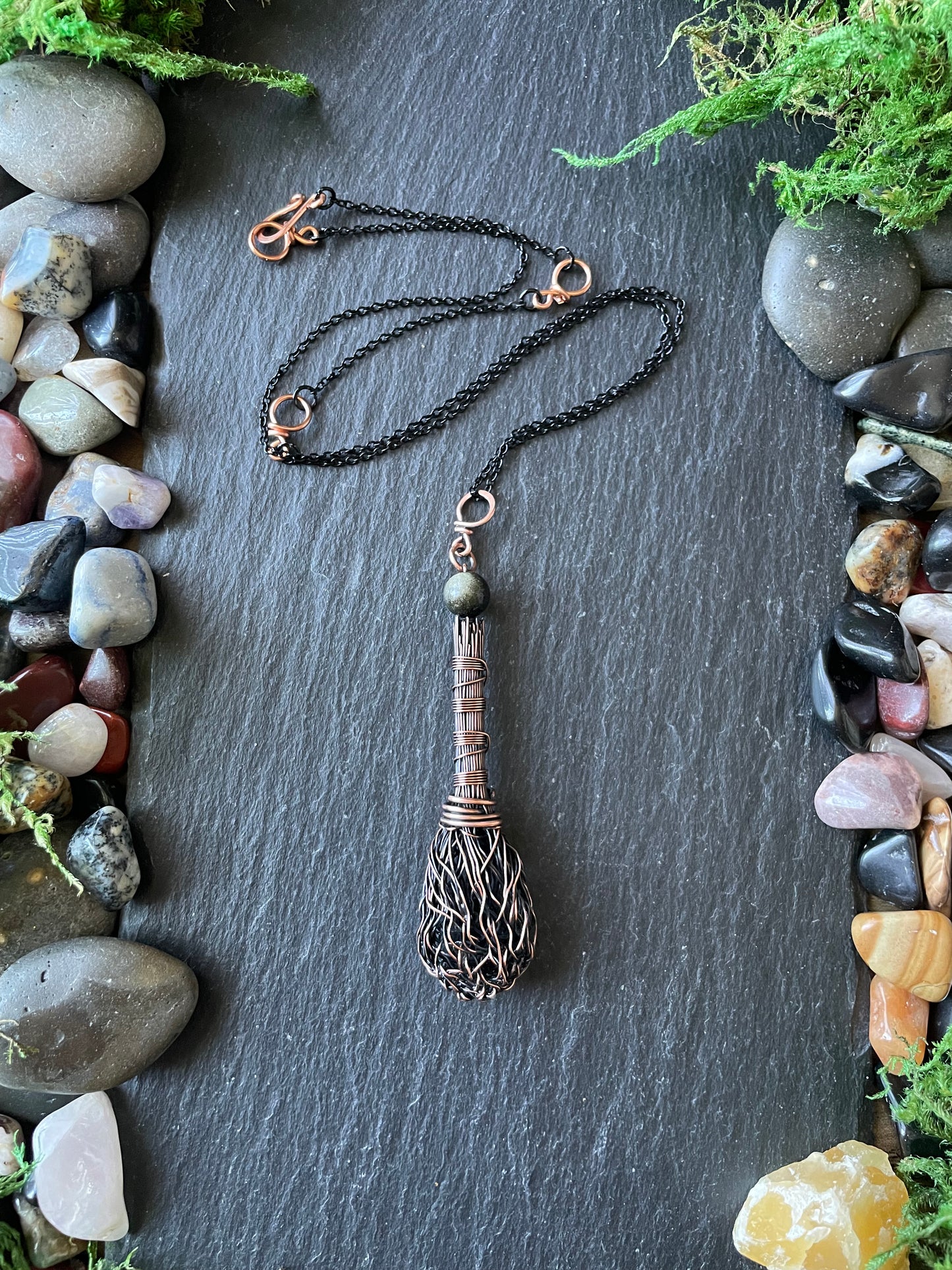 Necklace with a decorative pendant on a dark surface with stones and plants.