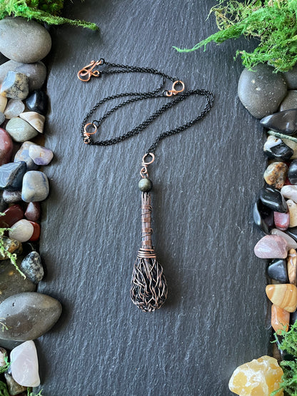 Necklace with a decorative pendant on a dark surface with stones and plants.