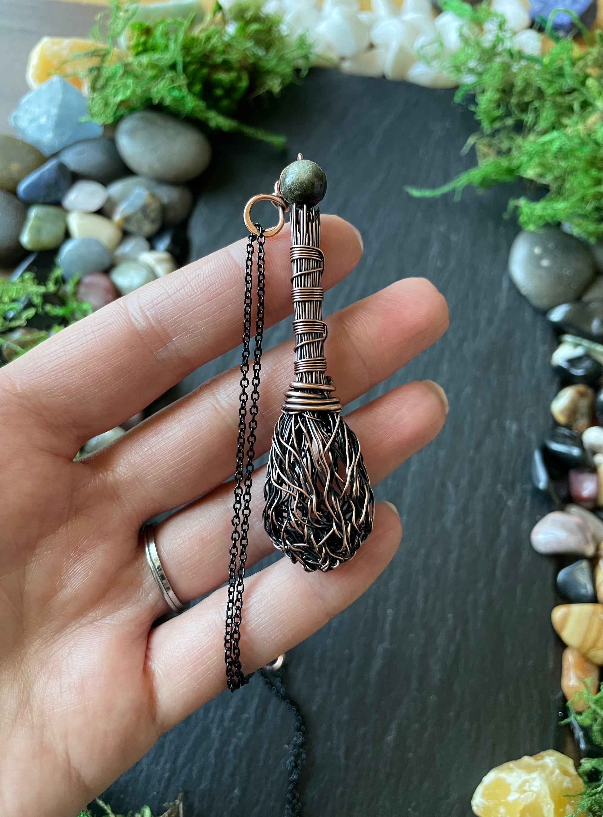 Hand holding a decorative necklace with a detailed pendant against a natural stone background