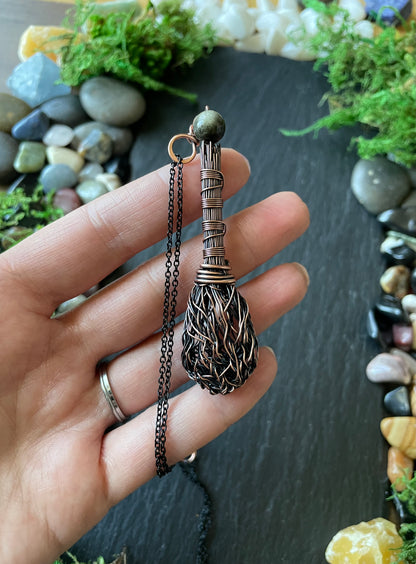 Hand holding a decorative necklace with a detailed pendant against a natural stone background