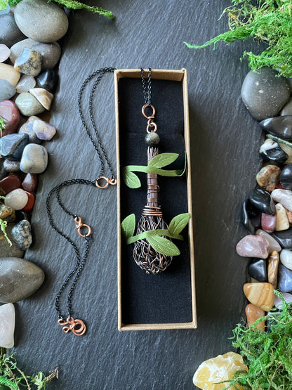 Copper broom necklace held in box with string on a stone surface