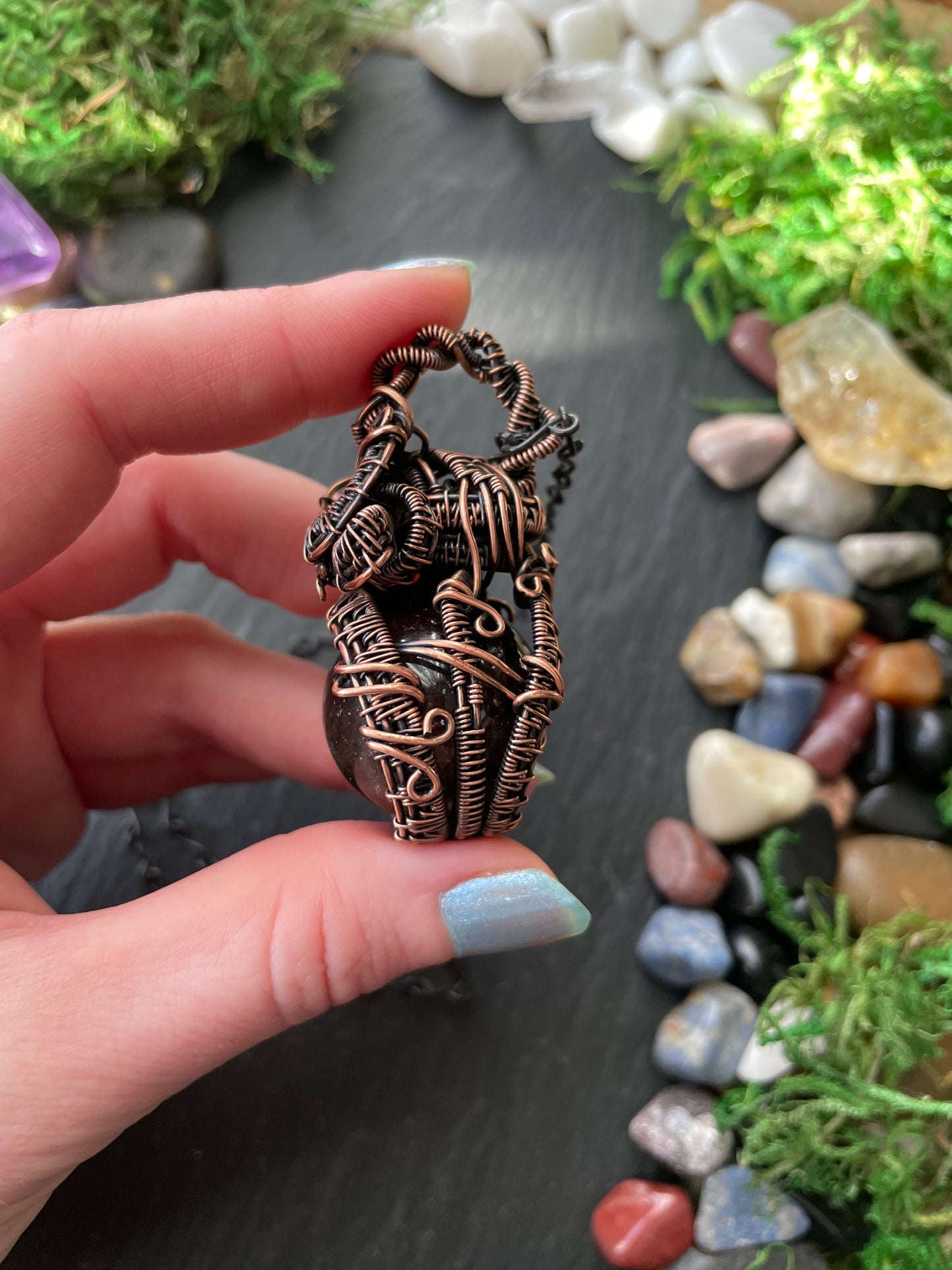 Hand holding a copper wire-wrapped crystal amulet with a natural stone background